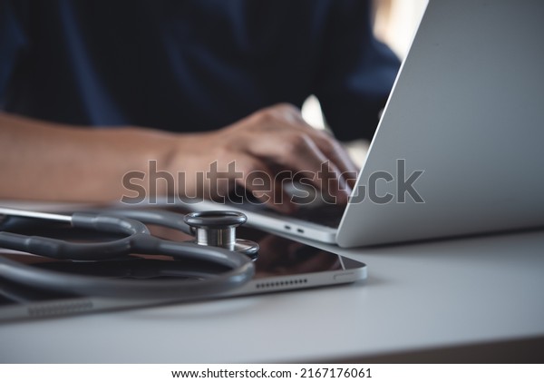 Close\
up of doctor, sugeon working on laptop computer with digital tablet\
on table in doctor\'s office, medical research, healthcare and\
medicine, electronic health record system\
concept
