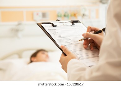 Close up of doctor writing on a medical chart with patient lying in a hospital bed - Powered by Shutterstock