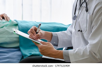 Close up of doctor writing on a medical chart with patient lying on hospital bed. Healthcare and insurance concept - Powered by Shutterstock