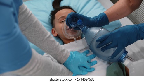 Close Up Of Doctors Doing Cardiopulmonary Resuscitation To Preteen African Kid In Hospital Ward. Medical Team Using Bag Valve Oxygen Mask Rescuing Unconscious Child