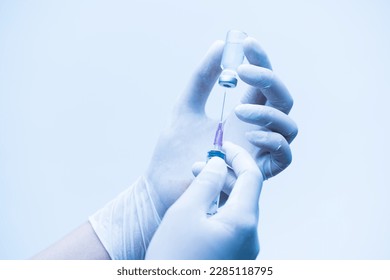 Cierre la mano del médico sujetando la botella y la jeringa para la vacuna a un paciente con un fondo de color azul.Enfermeras con jeringuillas son vacunas para el paciente para la protección contra la gripe.Tratamiento de medicamentos.