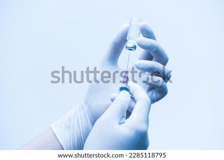 Close up doctor's hand holding medicine bottle and syringe for vaccine to patient on blue tone background.Nurse using syringe are vaccination to patient for influenza protection.Medication treatment.