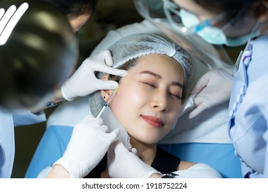 Close Up Of Doctor's Hands In Gloves Doing Injections Of Botulinum Toxin On Young Asian Female Patient Face Laying On Bed While Nurse's Hands Holding Ice Pack Tapping On The Area Just Injected.