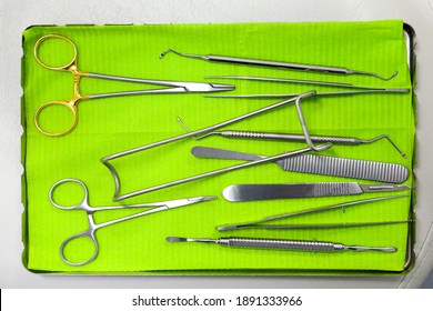 A Close Up Of Doctors Tools On A Metal Tray With Green Paper