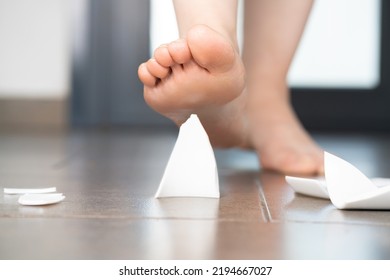 Close Up Of A Domestic Accident Of Woman Bare Foot Stepping On Broken Glass Of A Plate On The Floor In The Kitchen At Home