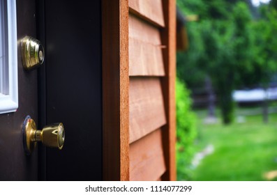 Close Up Of A Door Knob And Dead Bolt With Cedar House Siding And A Lawn In The Background