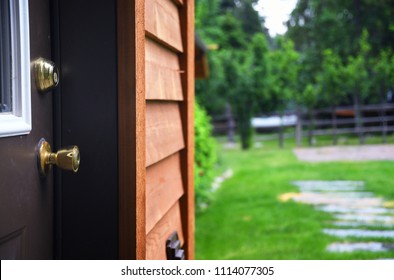 Close up of a door knob and dead bolt with cedar house siding and a lawn in the background