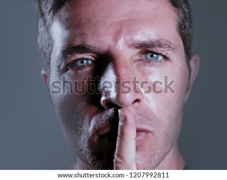 close up dramatic studio portrait of young handsome and attractive man with finger on his closed mouth warning to shut up and not to speak in censorship and freedom of speech coercion