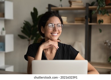 Close up dreamy smiling businesswoman in glasses distracted from laptop, looking to aside, pensive young woman visualizing good future, dreaming about new opportunities, pondering project strategy