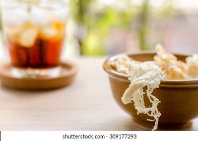 close up in dried squid and cola in glass on wooden background