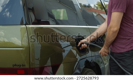 Close up of driver attaching electric cable connector to electric SUV car to recharge battery before long trip. Man opens vehicle inlet port of EV automobile to do refill using green electricity