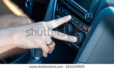 Close up of a driver hand adjusting climate control and air conditioning in a modern car. Vehicle dashboard with temperature controls and infotainment panel.