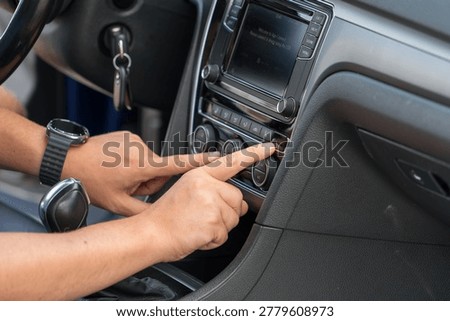 Close up of driver hands adjusting climate control buttons on modern car dashboard with multimedia system and gear shifter.