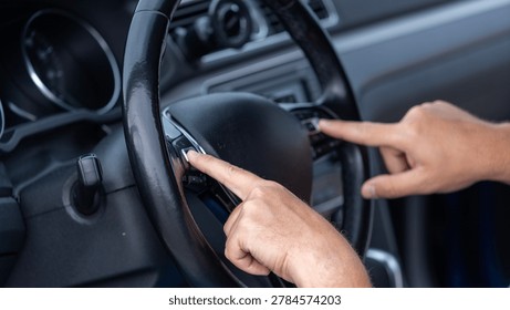 Close up of driver hands pressing steering wheel control buttons inside modern vehicle with multimedia and cruise control system.