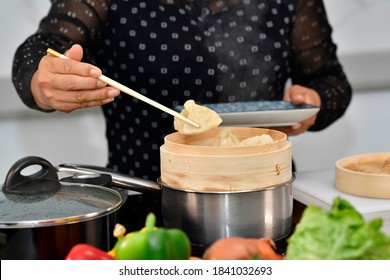 Close up of a dumpling being picked up from a bamboo steamer by a female hand using chopsticks. Traditional chinese food and cooking concept.