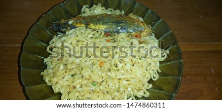 Close up eat fried instant noodle or mie mee goreng on plate, isolated on white background, orange yellow color, wavy flat texture, heap pile vast frame. Served on plate wood table with ikan pindang
