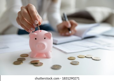 Close up of economical young woman manage household family budget calculate finances at home. Provident female put coin in piggy bank saving invest money for future payment. Investment concept. - Shutterstock ID 1831290271
