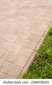 Close Up Of Edge Of New Sidewalk And Green Grass Near It. Park Path Made Of Light Concrete Blocks Of Different Shapes And Overgrown Grass In Park Area. Nobody.