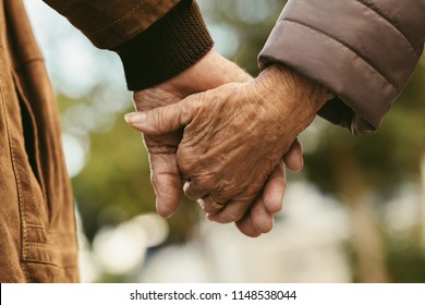 Close up of elderly couple holding hands and walking outdoors. Rear view of man and woman holding hands of each other while walking outdoors.