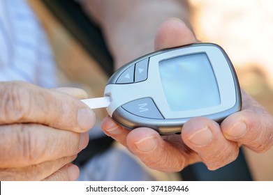 Close Up Of Elderly Man's Hands Measuring His Blood Sugar With A Blood Sugar Monitor. This Is One Of A Six Picture Series. In This Picture He Inserts The Disposable Test Strip Into The Monitor 