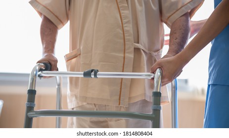 Close up of elderly patient hands using walking frame with nurse assistance. Medical professional or caregiver assisting senior man to walk with walker during recovery in hospital. 