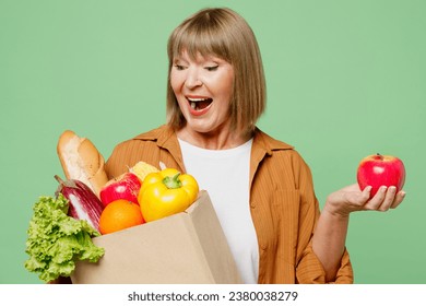 Close up elderly smiling happy fun woman wear brown shirt casual clothes hold in hand apple fruit shopping paper bag with food products isolated on plain green background. Delivery service from shop - Powered by Shutterstock