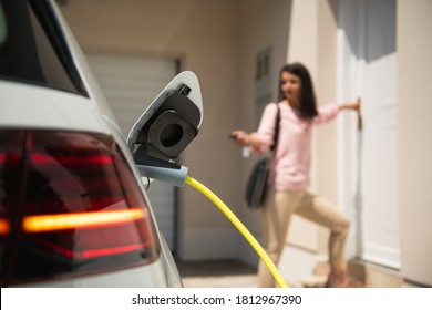 Close up of a electric car charger with female silhouette in the background, entering the home door and locking car - Shutterstock ID 1812967390