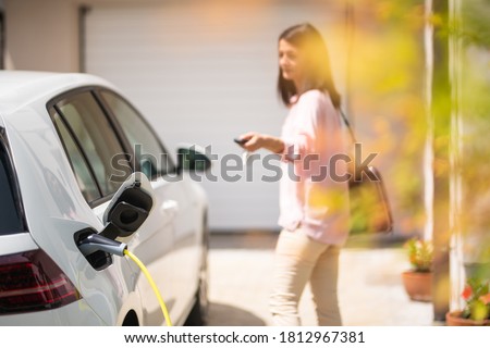 Close up of a electric car charger with female silhouette in the background, locking a car