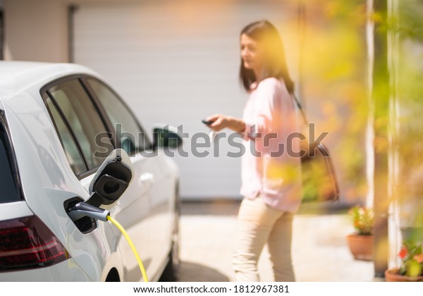 Close up of a electric car\
charger with female silhouette in the background, locking a\
car