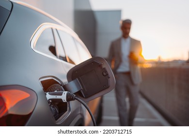 Close up of electric car charging, businessman standing in background and waiting.