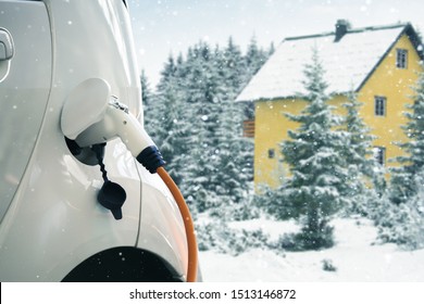 Close Up Of Electric Car With A Connected Charging Cable On The Blurred Background Of A Winter House.