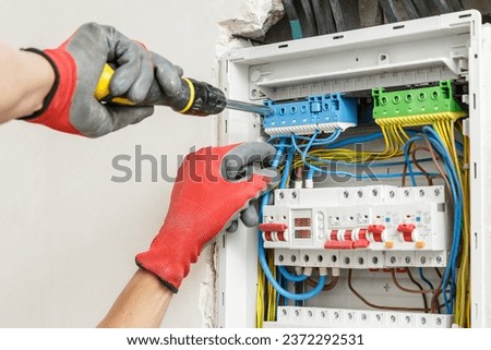 Close up of electrician's hands in working gloves installing and maintainin electrical junction box. Electrical services concept  