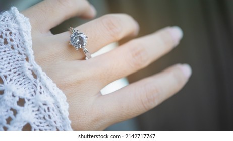 Close up of an elegant diamond ring on woman finger with window and sunlight background. love and wedding concept. Soft and selective focus.
