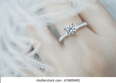 Close up of elegant diamond ring on the finger with feather and gray Scarf background. Diamond ring.