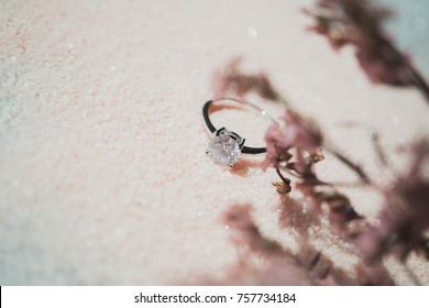 Close up of an elegant diamond ring on the pink sand and pink dried flower background. love and wedding concept.(soft and selective focus)