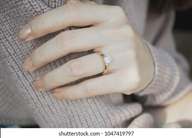 Close Up Of An Elegant Engagement Diamond Ring On Woman Finger With Dark Pink Sweater Winter Clothe. Love And Wedding Concept.soft And Selective Focus.