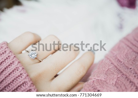 Close up of an elegant engagement diamond ring on woman finger with dark pink sweater winter clothe. love and wedding concept.