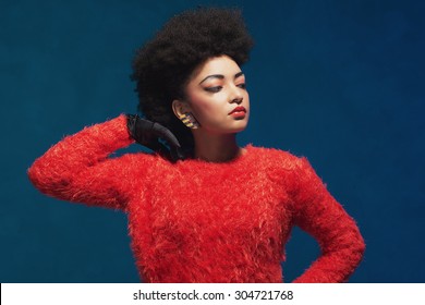 Close Up Elegant Young Woman With Afro Hairstyle, Wearing Fashionable Fuzzy Tops, Looking To The Right Frame With Hand On Her Hair. Isolated On Blue Background.