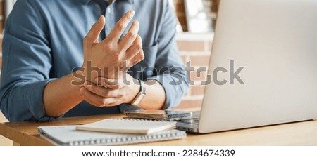 close up employee man massage on his hand and arm for relief pain from hard working on the desktop table at hoe office for stiff or cramp symptom or carpal tunnel syndrome concept