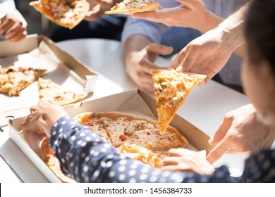 Close up of employees have break in office eating  pizza from takeaway delivery, happy workers enjoy tasting Italian food, spend dinner together, colleagues celebrate at workplace with fastfood