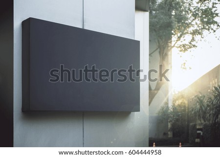 Close up of empty black poster on concrete building. Trees and sunlight in the background. Mock up