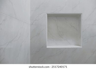 Close up of empty built-in shower caddy in wall recess in bathroom. Modern elegant bathroom interior with marble wall tiles. Display shelf for toiletries logo branding mockup.