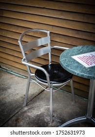 Close Up Of An Empty Chair And Table With Warning Note Saying That Please Do Not Move The Tables Or Chairs. There Should Be 1 Person On Either Side Of The Table.