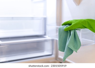 Close up of empty and clean refrigerator after defrosting. Person hand in rubber glove with textile on plastic fridge box. Housework concept. Copy space