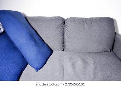 Close up empty gray sofa with two blue pillows isolated on horizontal white wall background.