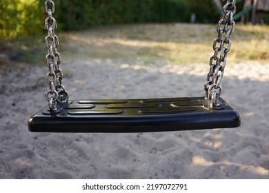 
Close Up Of An Empty Swing In A Playground. Sandbox And Blurred Background. No People. Children's Playground Or Kindergarten