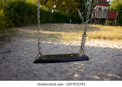 
Close Up Of An Empty Swing In A Playground. Sandbox And Blurred Background. No People. Children's Playground Or Kindergarten