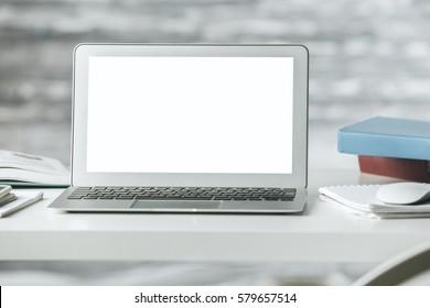 Close Up Of Empty White Laptop Screen, Books And Other Items On Light Desktop. Blurry Wooden Background. Mock Up