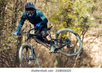 Close up of Enduro mtb rider jumping down the mtb track by bikepark in the mountains of the Pyrenees in Catalonia. With full face helmet, goggles, cycling gear and winter protections.