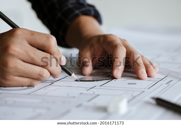 Close up of engineer drawing on blueprint\
architectural project at a desk in the office. inspection workplace\
for architectural plan, sketching a construction project.\
Construction concept